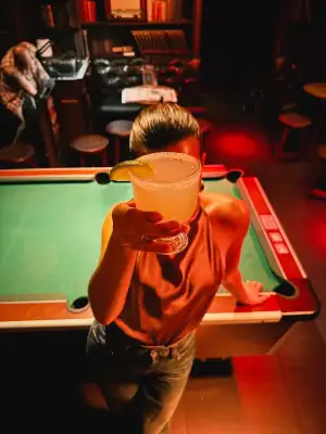 Une personne appuyée sur le billard vert, un cocktail à la main
